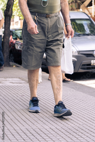 Man in bermuda shorts walking down the street with a bag with purchases.