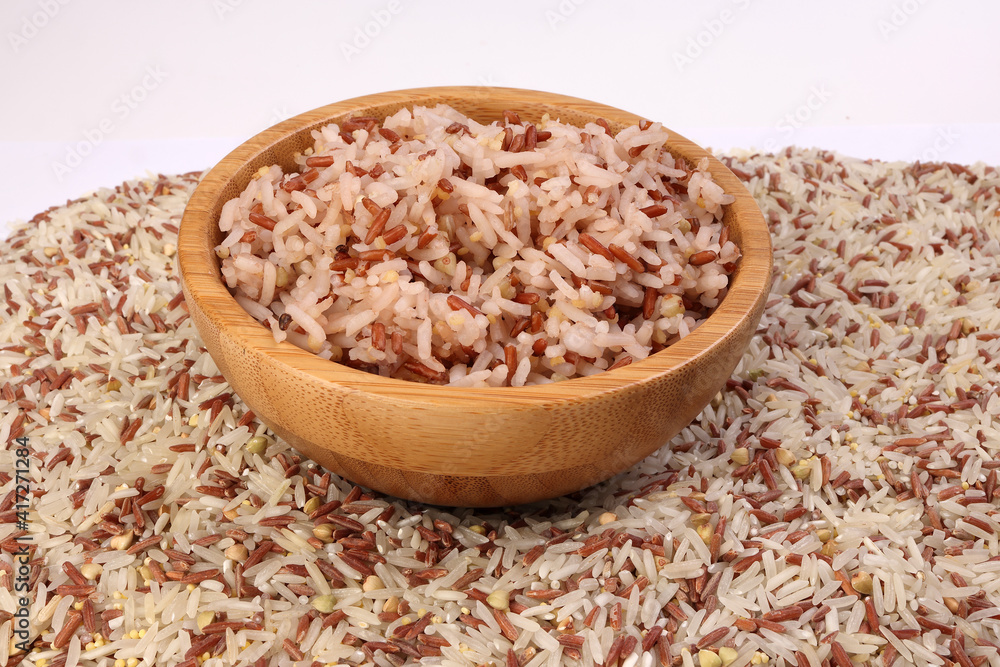 Cooked and raw mixed low glycaemic index healthy rice grain basmati millet buckwheat red rice in wooden bowl bed of rice over white background Cooked and raw mixed low glycaemic index healthy rice grain basmati millet buckwheat red rice in wooden bowl bed of rice over white background