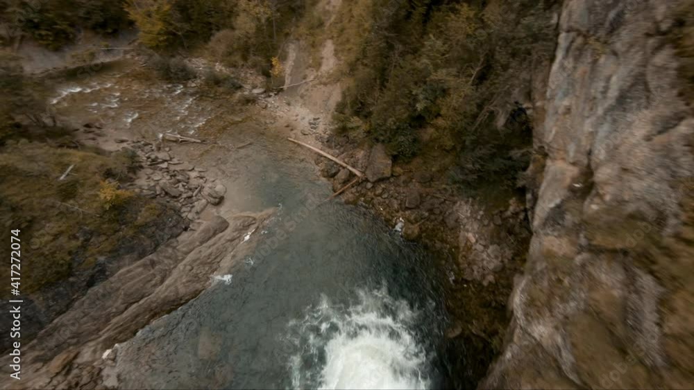 Cinematic aerial view over a stream and waterfall flowing through a autumnal forest, in a mountain valley Cinematic aerial view over a stream and waterfall flowing through a autumnal forest, in a mountain valley