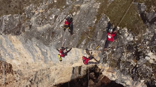 Rock climbers hanging on ropes from the edge of a rocky mountain drilling the rocks drone shot. photo
