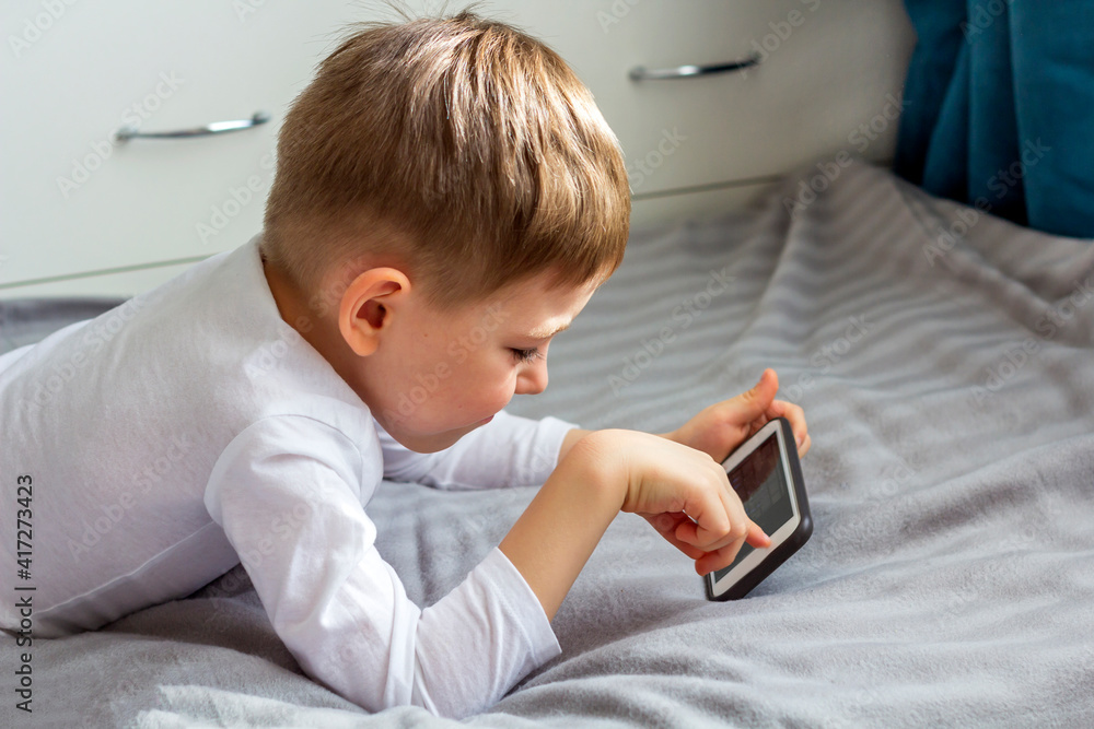 Happy kid (boy) make video call (via video chat) by smartphone to his dad, mom, grandpa, grandma. Stay home, social distance and self-isolation during quarantine concept. Selective focus, backlight