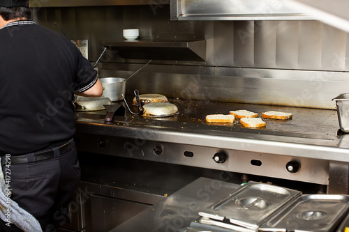 Foto A view of a line cook attending a stove and griddle area