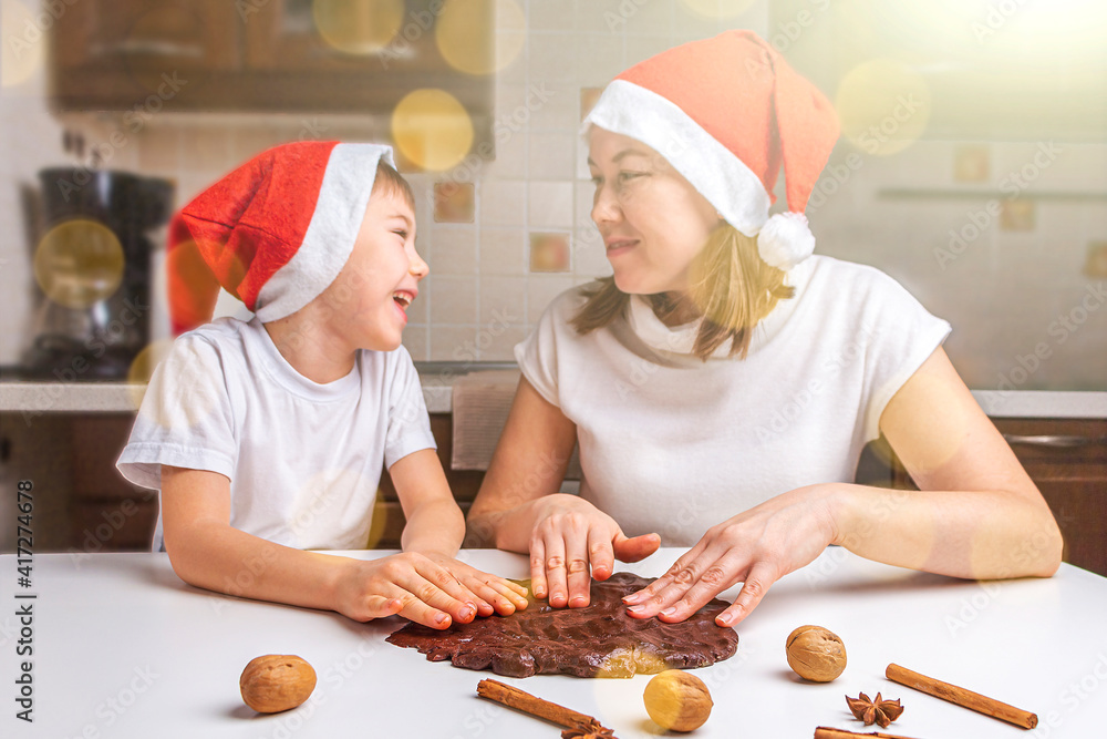 Cooking Christmas and New Year chocolate cookies or gingerbread. Traditional festive baking, bake with kids. Mom and son in santa hats knead dough. Holiday atmosphere, bokeh, Cooking Christmas and New Year chocolate cookies or gingerbread. Traditional festive baking, bake with kids. Mom and son in santa hats knead dough. Holiday atmosphere, bokeh,