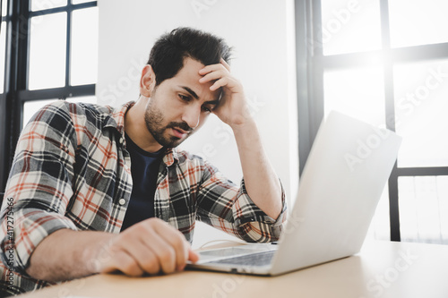 Iranian young man seriously working on computer laptop. He thinking find solution problem of work