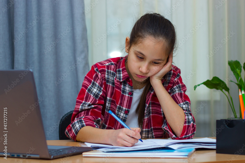 Sad brunette girl dressed in a red shirt, sitting at home studying, writes homework, communicates on the Internet. Sad brunette girl dressed in a red shirt, sitting at home studying, writes homework, communicates on the Internet.