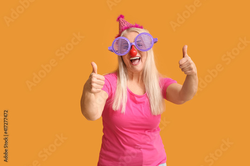 Φωτογραφία Mature woman in funny disguise showing thumb-up on color background