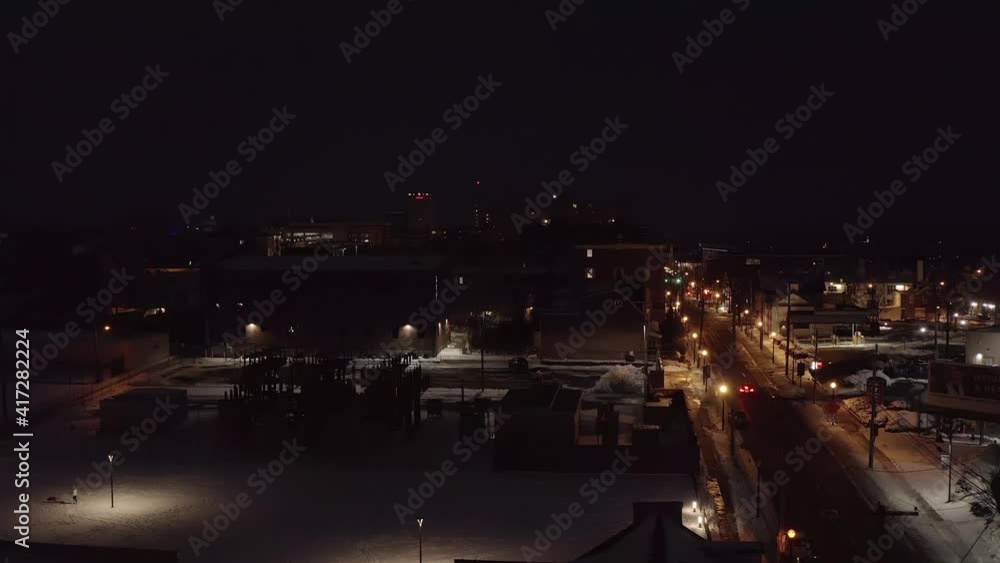 Car with red brake lights drives on quiet street during black night. White snow on ground. Aerial drone shot. Car with red brake lights drives on quiet street during black night. White snow on ground. Aerial drone shot.