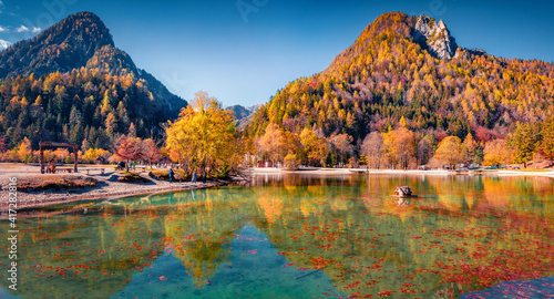 Beautiful autumn scenery. Fallen red beech leaf floats on the calm surface of the lake water. Sunny morning view of Jasna lake. Wonderful autumn scene of Julian Alps, Slovenia, Europe.