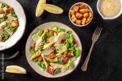Caesar salad with grilled chicken, romaine and Parmesan, shot from the top on a black background with copy space