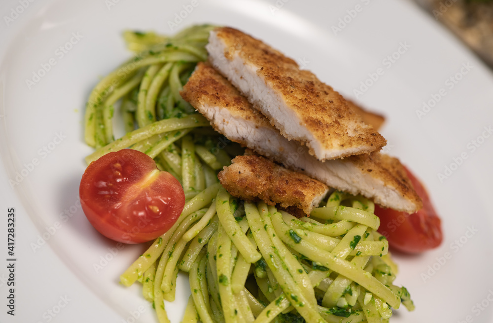 Turkey cutlet and Green spinach spaghetti with cheese and tomato on table