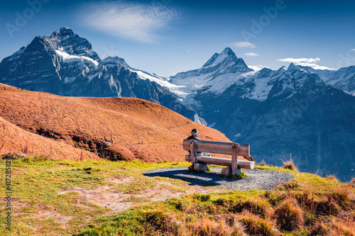 Tourist siting on the shore of Bachalp lake (Bachalpsee), Switzerland. Majestic autumn scene of Swiss alps, Grindelwald, Bernese Oberland, Europe. Beauty of nature concept background.