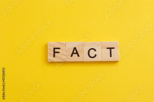 Word FACT made from wooden letters on yellow background.