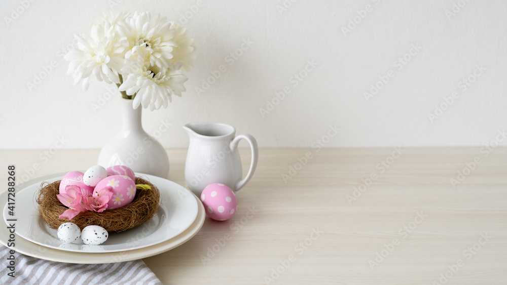 Easter dinner. Festive table. Holiday celebration. Banquet service. Pink color painted eggs in nest served in plate with white Spring flower bouquet arrangement on light copy space background. Easter dinner. Festive table. Holiday celebration. Banquet service. Pink color painted eggs in nest served in plate with white Spring flower bouquet arrangement on light copy space background.