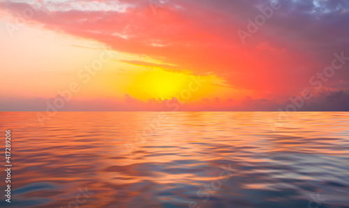 A beautiful sunset over the calm sea with red and orange clouds reflecting in the water © muratart