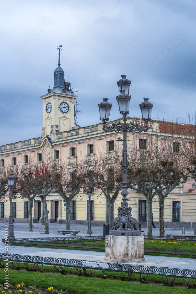 Fototapeta premium Plaza de Cervantes in the historic center of Alcalá de Henares. Detail of a street lamp in the foreground, and town hall tower in the background, on a winter morning. Vertical view.