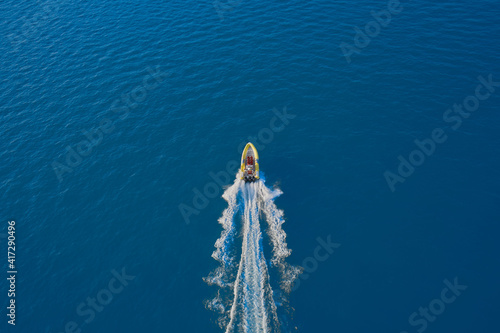 Drone view of a boat sailing at high speed. Aerial view of a boat in motion on blue water. Top view of a white boat sailing in the blue sea. luxury motor boat. © Berg