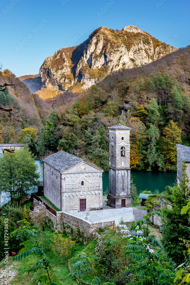 The ancient church of San Jacopo and behind the dam on the lake of Isola Santa, Careggine, Italy, nestled between the mountains of the Garfagnana