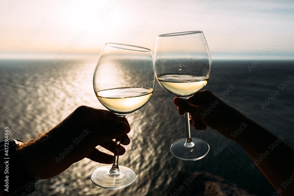 Hand holding glass of wine over the sea. Chin-chin. Romantic vacation. Two hands holding wine glasses against the sea. Copy space