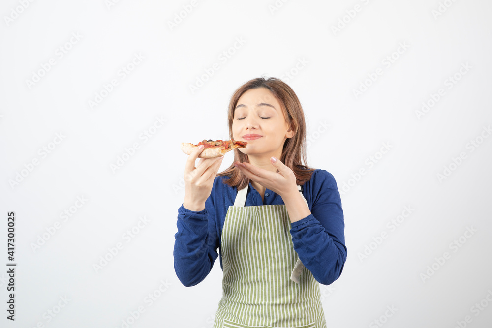 Portrait of young woman in apron eating pizza on white background Portrait of young woman in apron eating pizza on white background