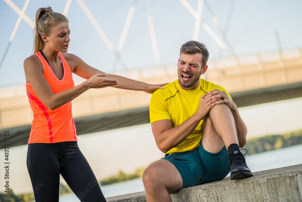Young couple is exercising outdoor. Man is having pain leg while warming up for jogging.