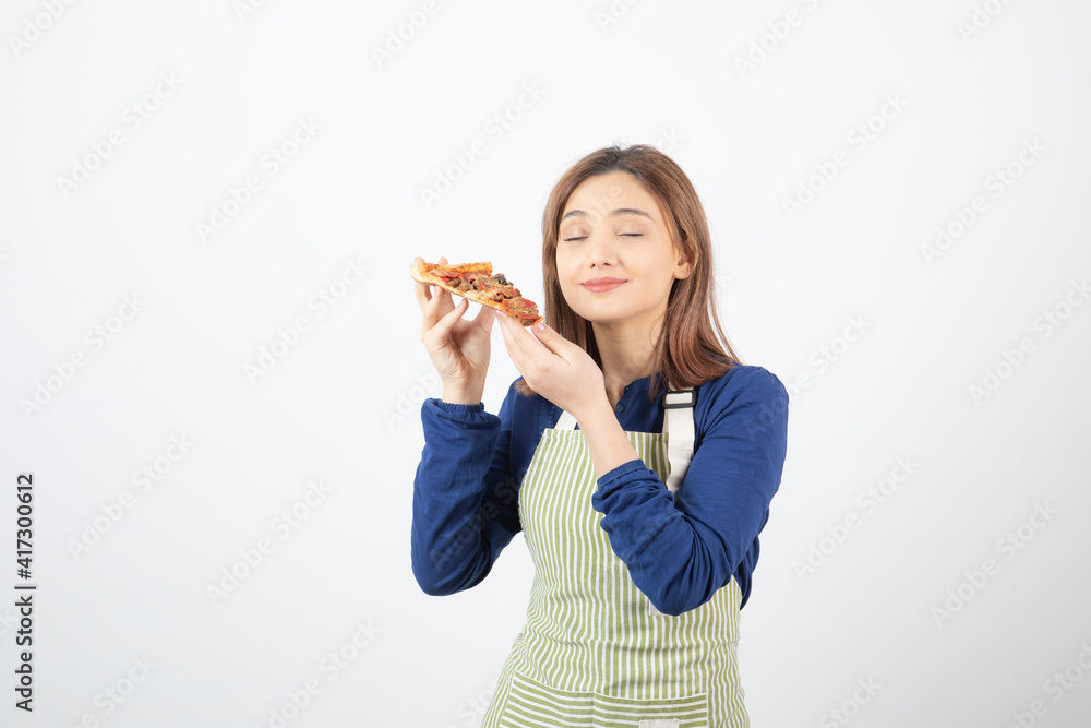 Portrait of woman in apron posing with slice of pizza on white background