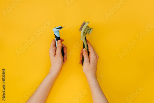 Female hands holding two different pet brushes for fur, on yellow background.