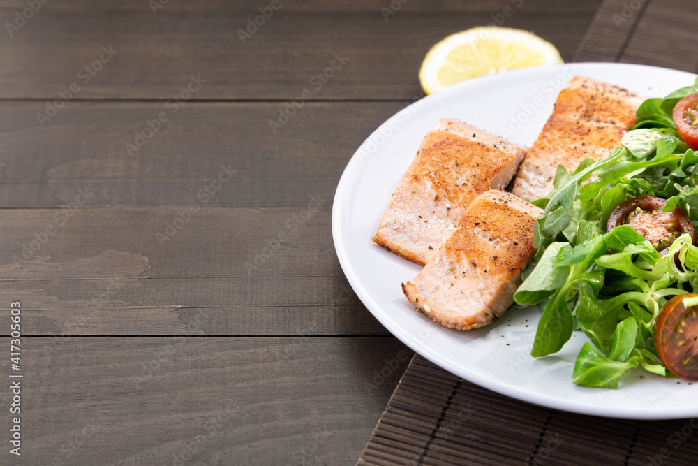 Salmon fillets on  white dish on dark wooden table with copyspace.