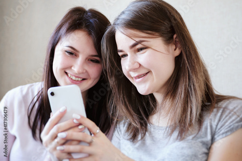 Two girlfriends are having fun and watching content in social networks on a mobile phone and using the internet wi-fi - Young women reading a text message or watching a video in a messenger.