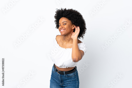 Young African American woman isolated on white background listening to something by putting hand on the ear