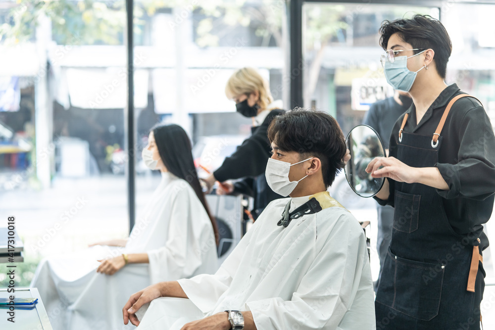 Professional male stylist cutting man's hair in salon. The man wearing mask and face shield to prevent from coronavirus infection during pandemic. New normal beauty salon or barber business concept. Professional male stylist cutting man's hair in salon. The man wearing mask and face shield to prevent from coronavirus infection during pandemic. New normal beauty salon or barber business concept.