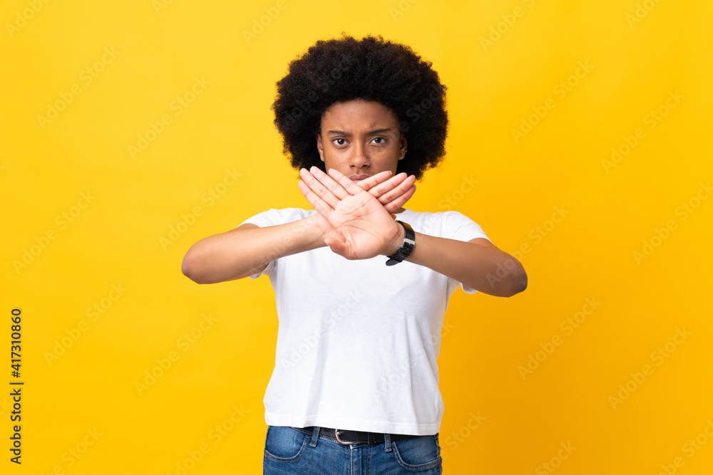 Young African American woman isolated on yellow background making stop gesture with her hand to stop an act Young African American woman isolated on yellow background making stop gesture with her hand to stop an act