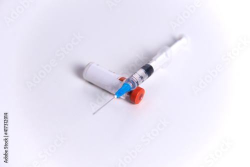 a bottle of vaccine, a syringe and a medical mask on a glass surface