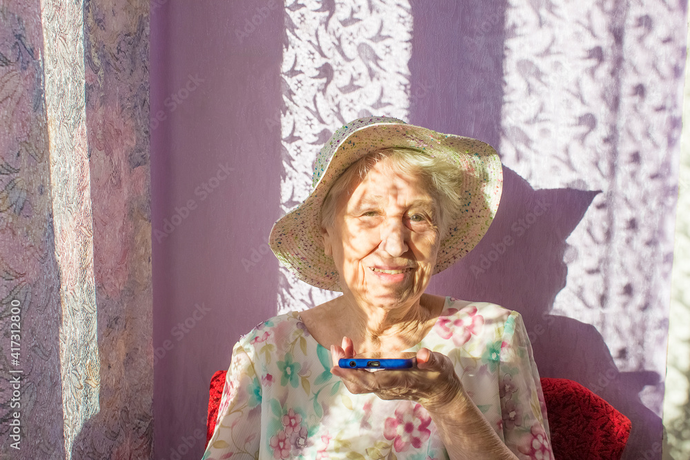 Charming elderly woman in rectangular black rimmed eyewear using voice recognition function on cell phone.