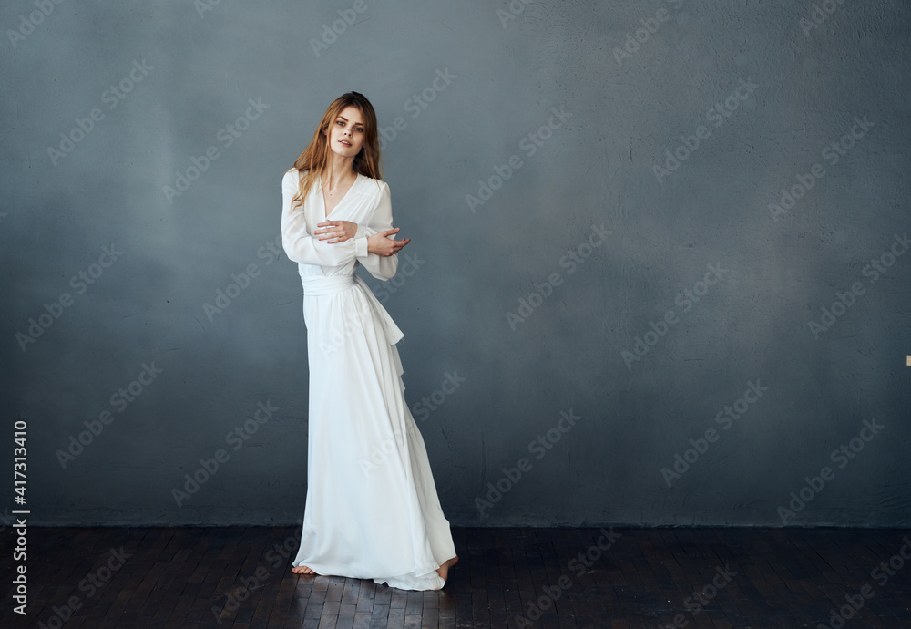 Romantic woman with red hair dances on a gray background in a white dress Romantic woman with red hair dances on a gray background in a white dress