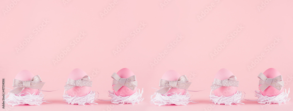 Fashion easter seamless banner - pink eggs with grey bows in white nest standing in row on pastel pink color.