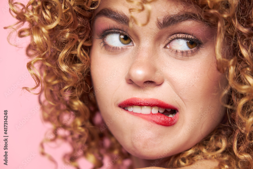 woman Curly hair grimace bites her lip with a look towards the pink background woman Curly hair grimace bites her lip with a look towards the pink background