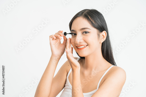 mixed race attractive asian woman putting mascara on eyelashes on white background