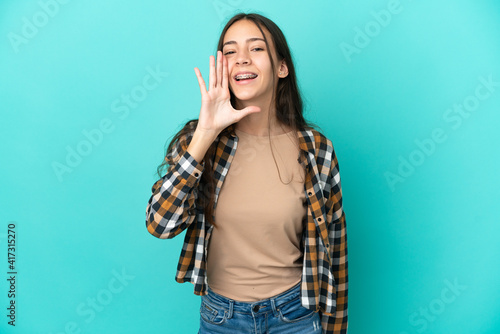Young French woman isolated on blue background shouting with mouth wide open © luismolinero