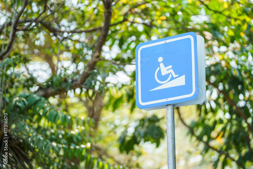Wheelchair symbol up the slope. Blue signboard for disabled wheelchairs to tell direction and get up in garden park background.