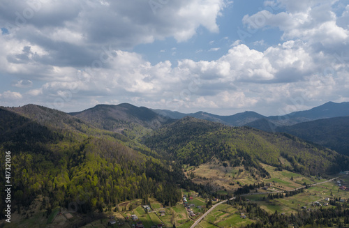Summer mountain landscape, beautiful scenery of Carpathian mountains in Western Ukraine. High mountain peaks, cloudy sky, green forests and a small village at the foot of the hill. Panoramic view.