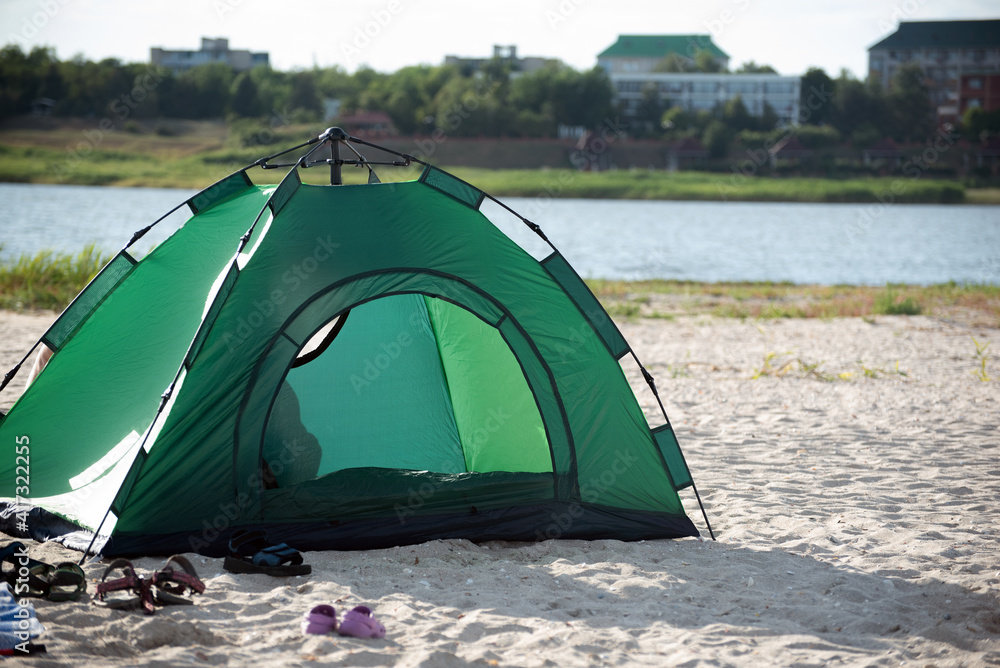 Green tent on river bank against city background. Camping. Leisure Green tent on river bank against city background. Camping. Leisure
