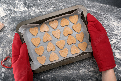 Chief in oven mitts holding freshly baked heart-shaped cookies. photo