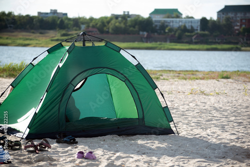 Green tent on river bank against city background. Camping. Leisure © somemeans