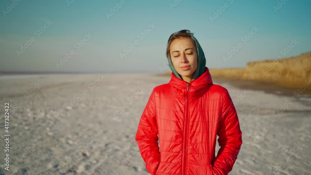 slow motion beautiful mixed raced woman hiker in hoodie walking along wide white beach at sunrise. millenial hipster girl in red jacket with wind blowing hair enjoing scenery landscape outdoors slow motion beautiful mixed raced woman hiker in hoodie walking along wide white beach at sunrise. millenial hipster girl in red jacket with wind blowing hair enjoing scenery landscape outdoors