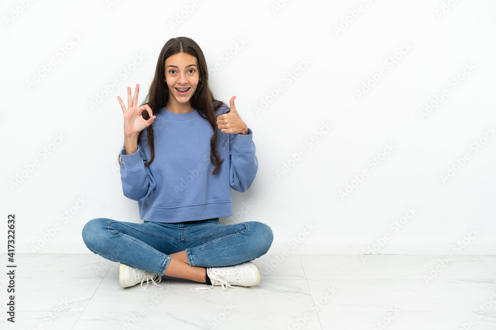 Young French girl sitting on the floor showing ok sign and thumb up gesture Young French girl sitting on the floor showing ok sign and thumb up gesture