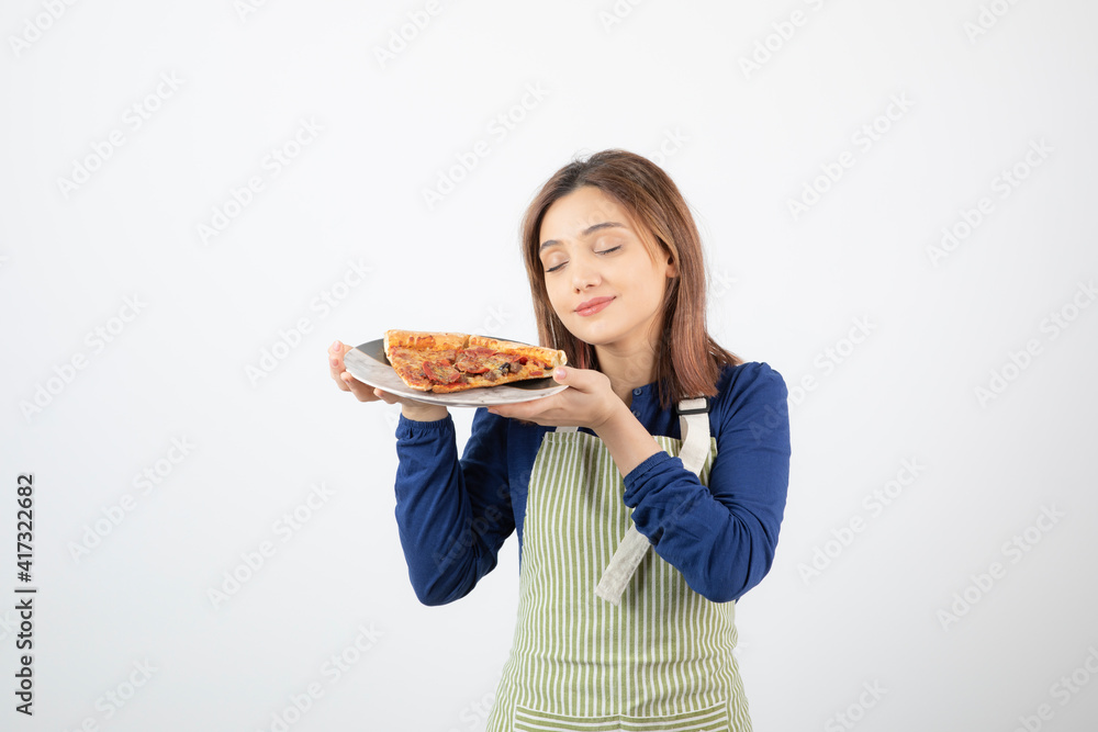 Portrait of woman in apron smells slice of pizza on white background Portrait of woman in apron smells slice of pizza on white background