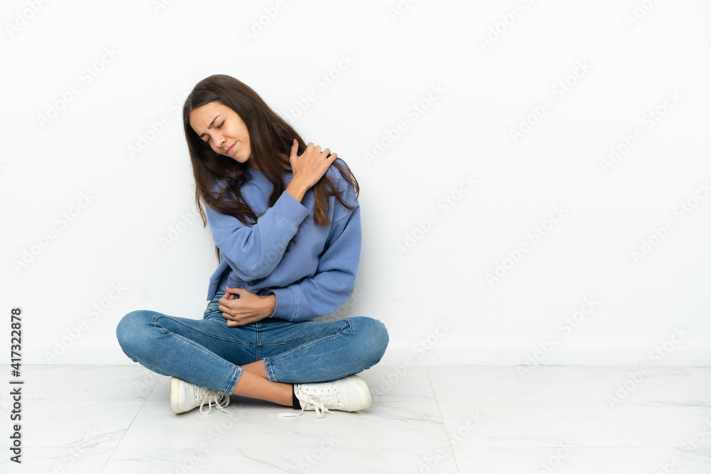 Young French girl sitting on the floor suffering from pain in shoulder for having made an effort Young French girl sitting on the floor suffering from pain in shoulder for having made an effort