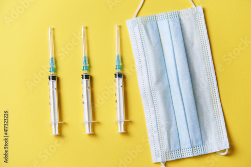 three syringes, a medical dressing, and vials for injecting the vaccine on a yellow background. 