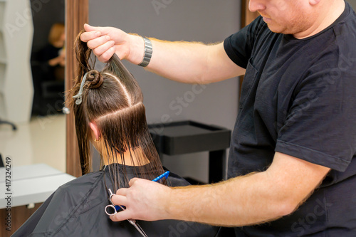 Male hairdresser holds and splits long hair of a young brunette woman in a hair salon