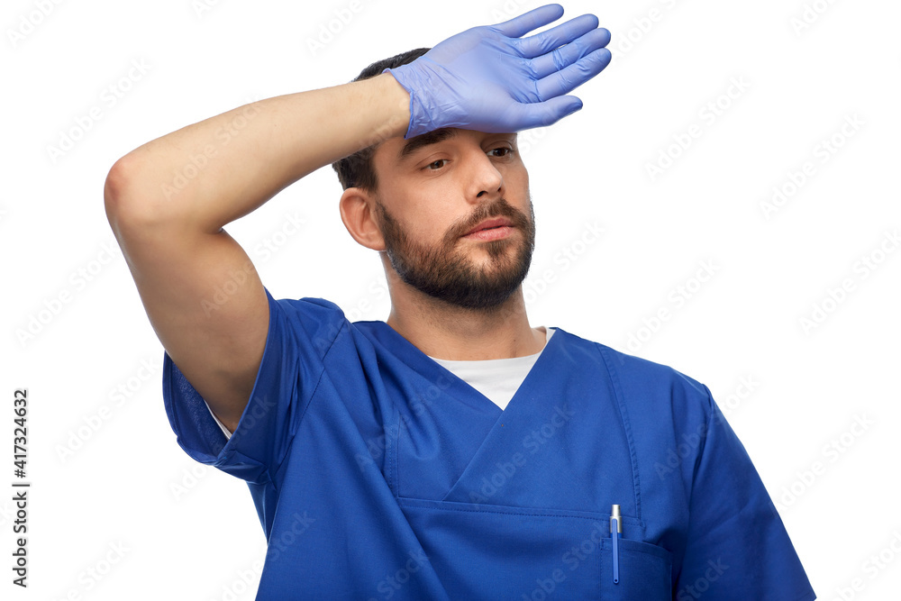 healthcare, profession and medicine concept - tired doctor or male nurse in blue uniform and medical gloves on over white background